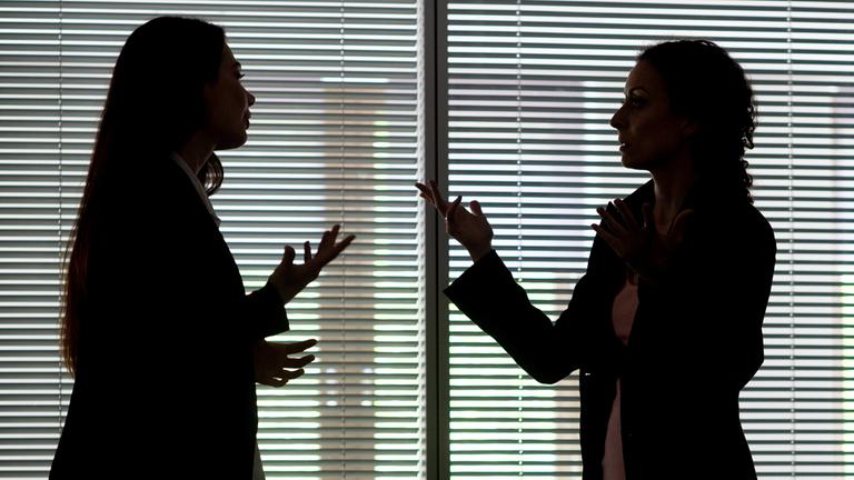 Zwei Frauen heben gestikulierend die Hände in die Höhe, während sie diskutieren.