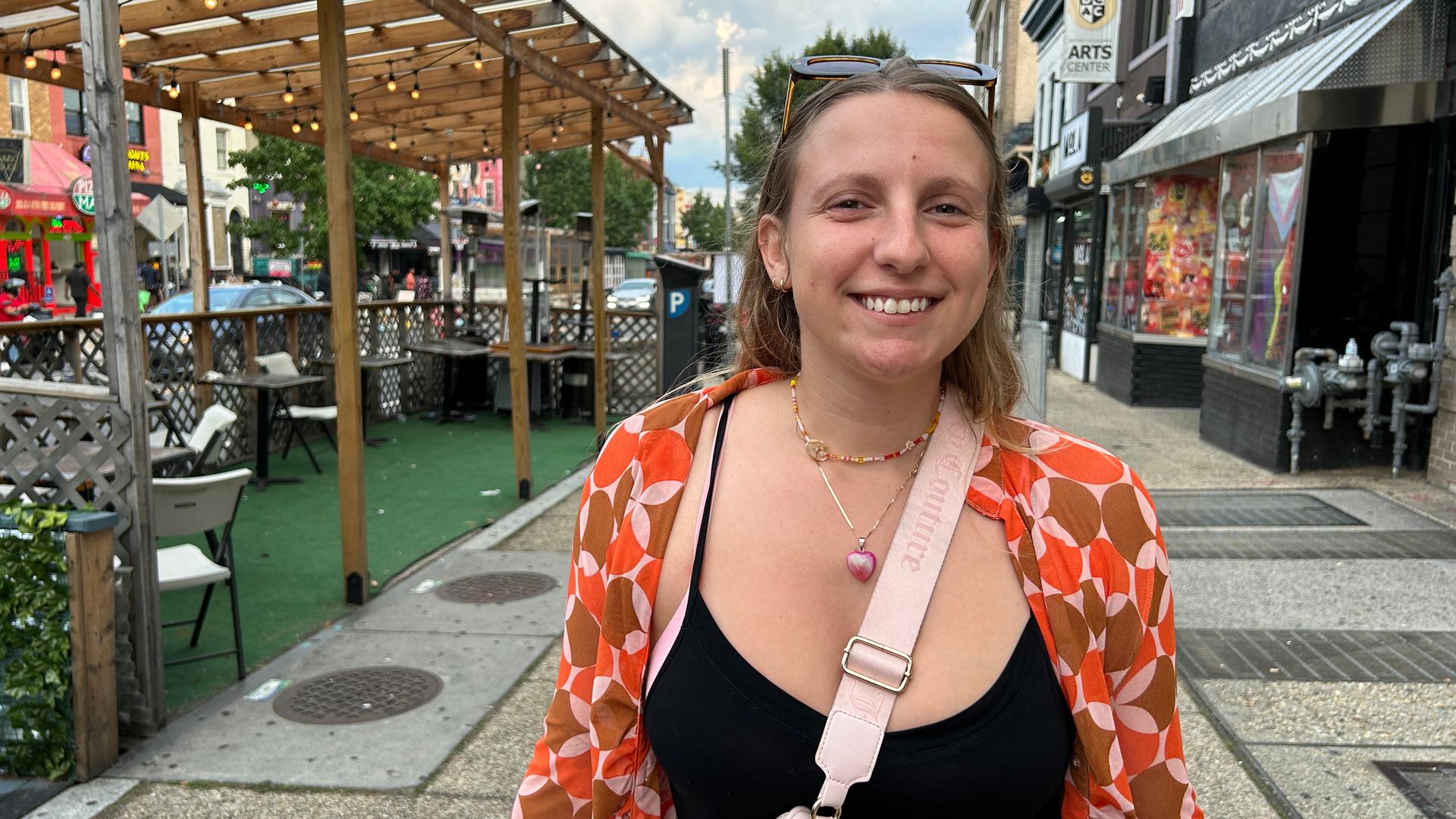 Eine junge Frau mit Sonnenbrille in den Haaren steht auf dem Bürgersteig.