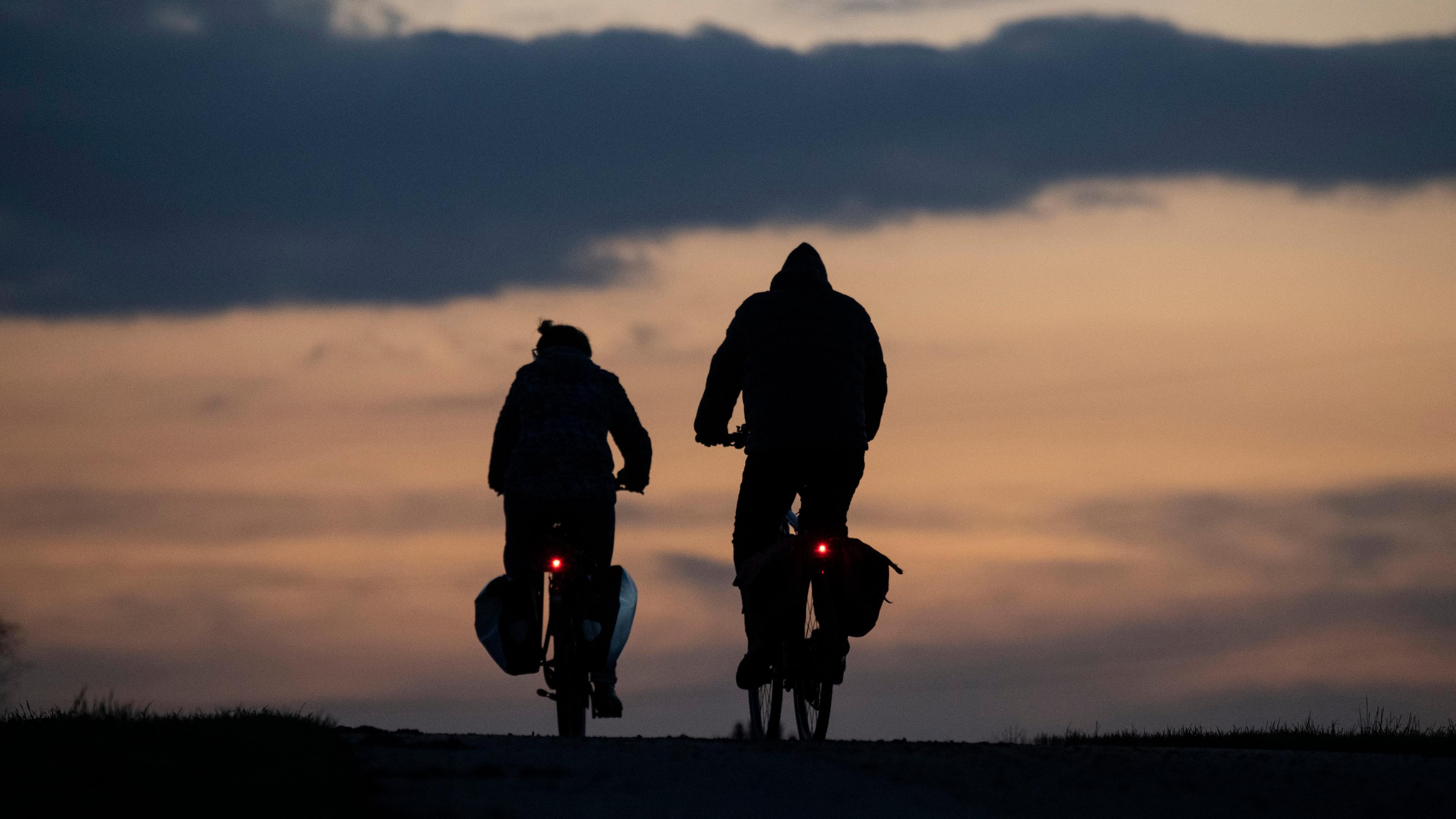 Man sieht zwei Radfahrende als Silhouette vor einem orangenen Himmel.