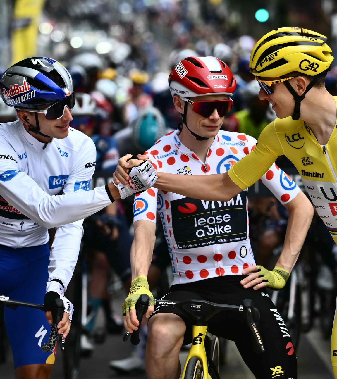 Florian Lipowitz schlägt seine Hand mit Tadej Pogacar ein während Jonas Vinegaard zwischen den beiden steht mit seinem Rad.
