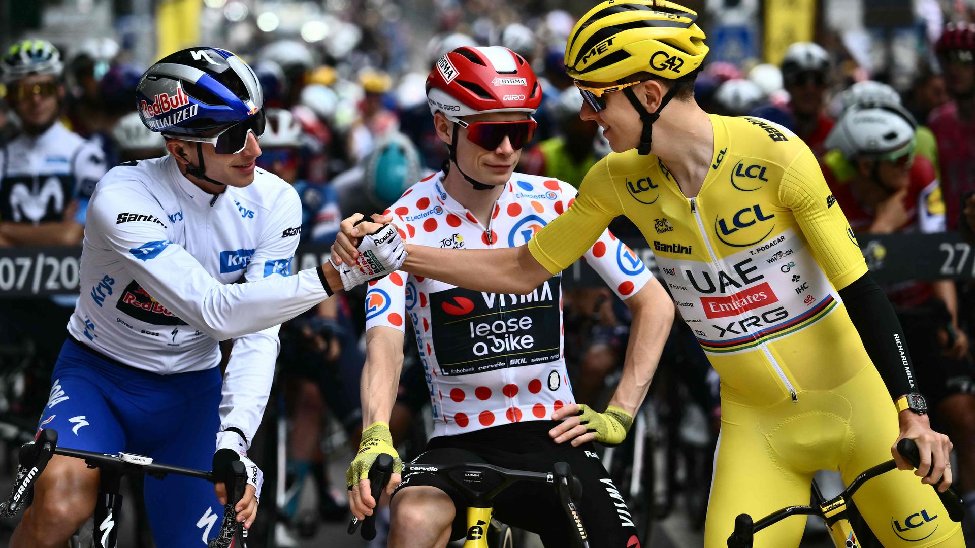 Florian Lipowitz schlägt seine Hand mit Tadej Pogacar ein während Jonas Vinegaard zwischen den beiden steht mit seinem Rad.