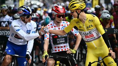 Florian Lipowitz schlägt seine Hand mit Tadej Pogacar ein während Jonas Vinegaard zwischen den beiden steht mit seinem Rad.