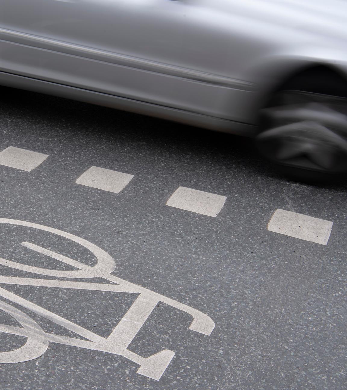 Auto fährt an Radweg vorbei. Seitentür zu sehen. 