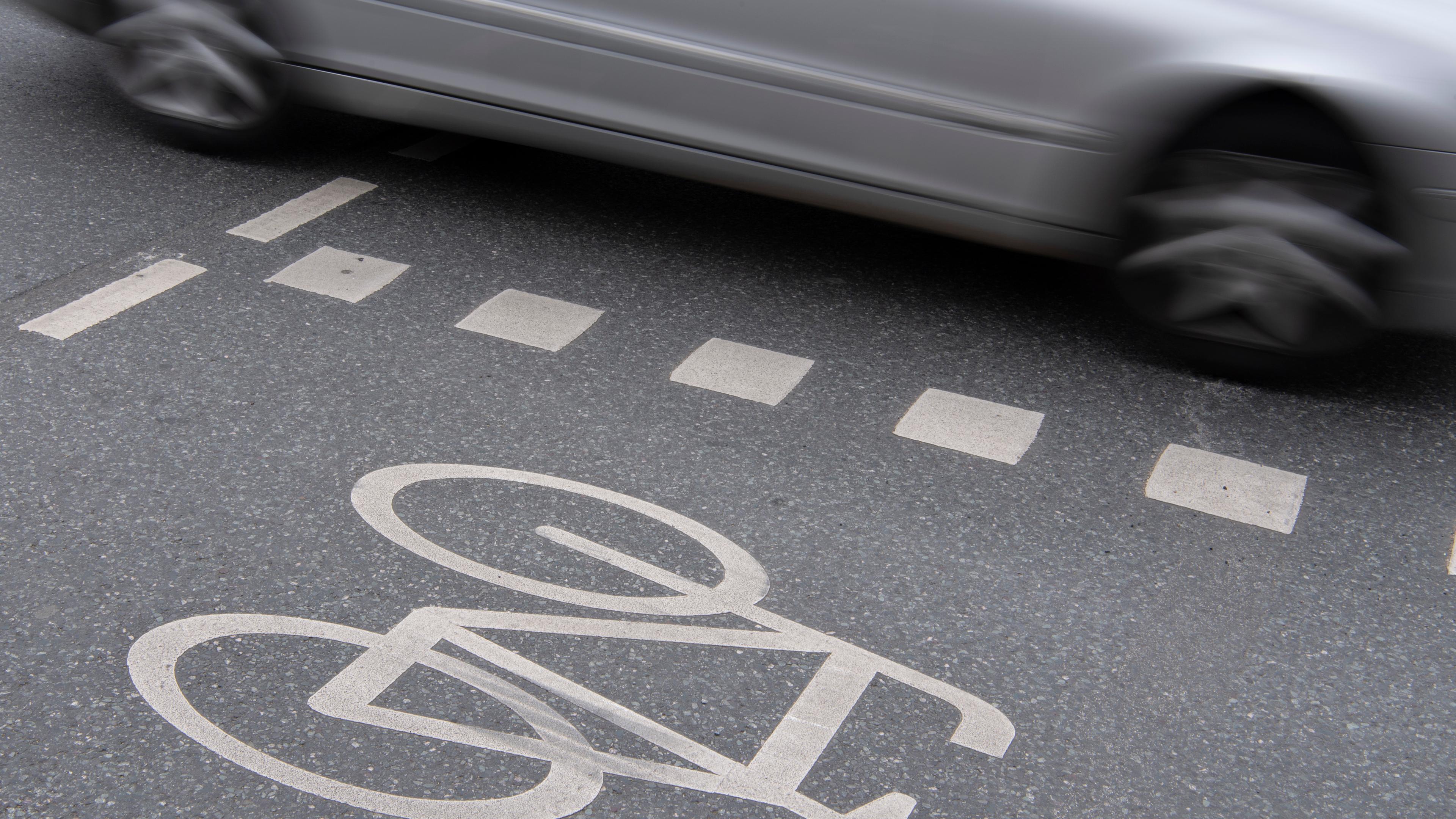Auto fährt an Radweg vorbei. Seitentür zu sehen. 