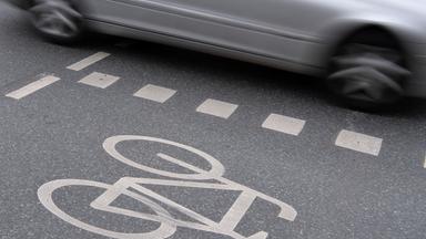 Auto fährt an Radweg vorbei. Seitentür zu sehen. 