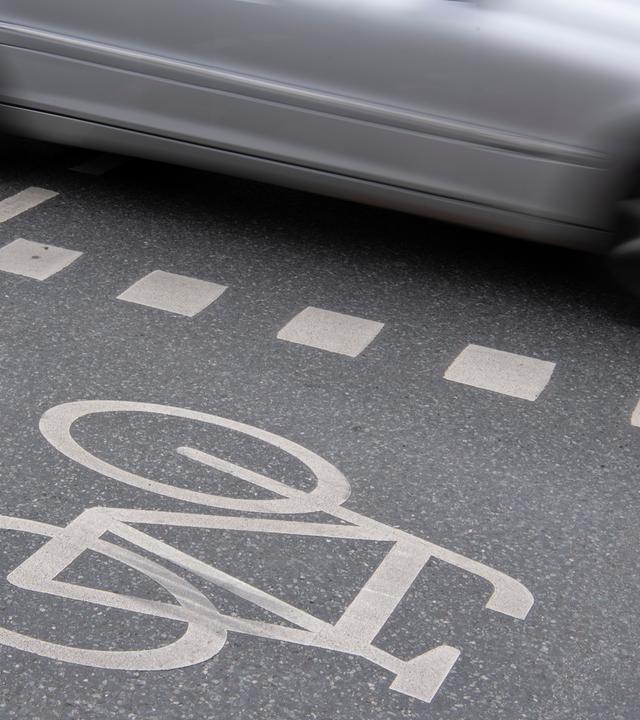Auto fährt an Radweg vorbei. Seitentür zu sehen. 