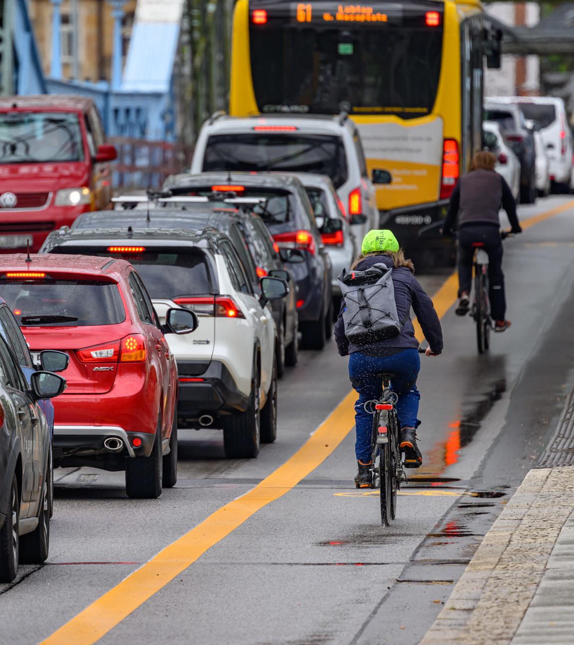 Radfahrer fahren an der Elbbrücke Blaues Wunder in Dresden auf einem markierten Radweg an Autos im Stau vorbei.