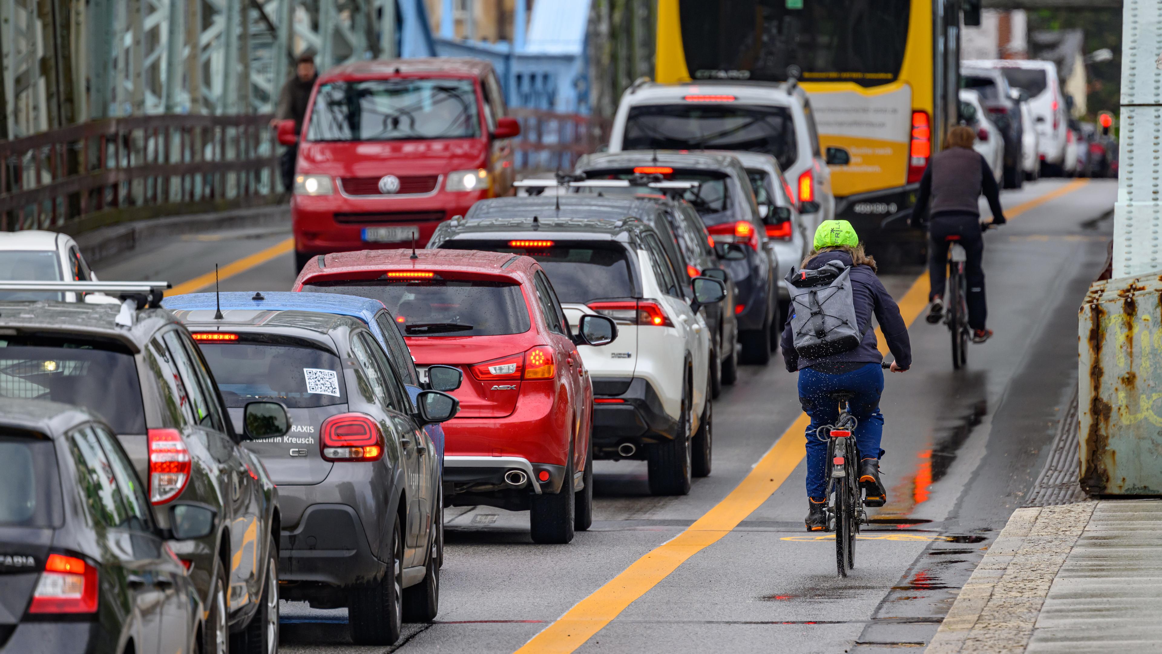 Radfahrer fahren an der Elbbrücke Blaues Wunder in Dresden auf einem markierten Radweg an Autos im Stau vorbei.