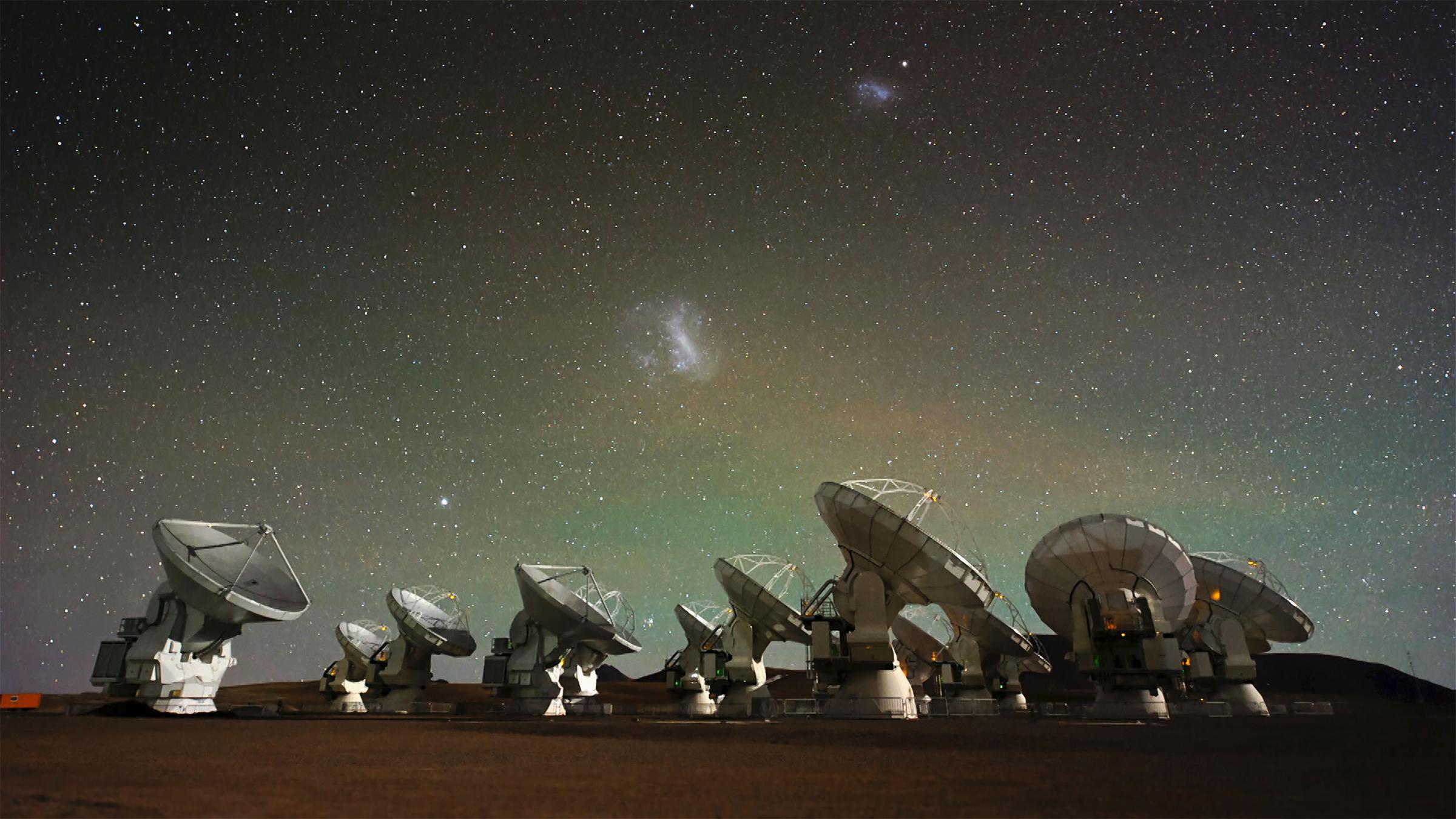 Mehrere Riesenteleskope, ausgerichtet auf den Himmel. Über ihnen sind die Sterne am Nachthimmel zu sehen.