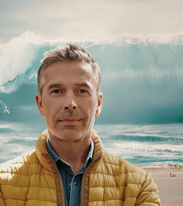Dirk Steffens im Vordergrund, riesige Welle im Hintergrund