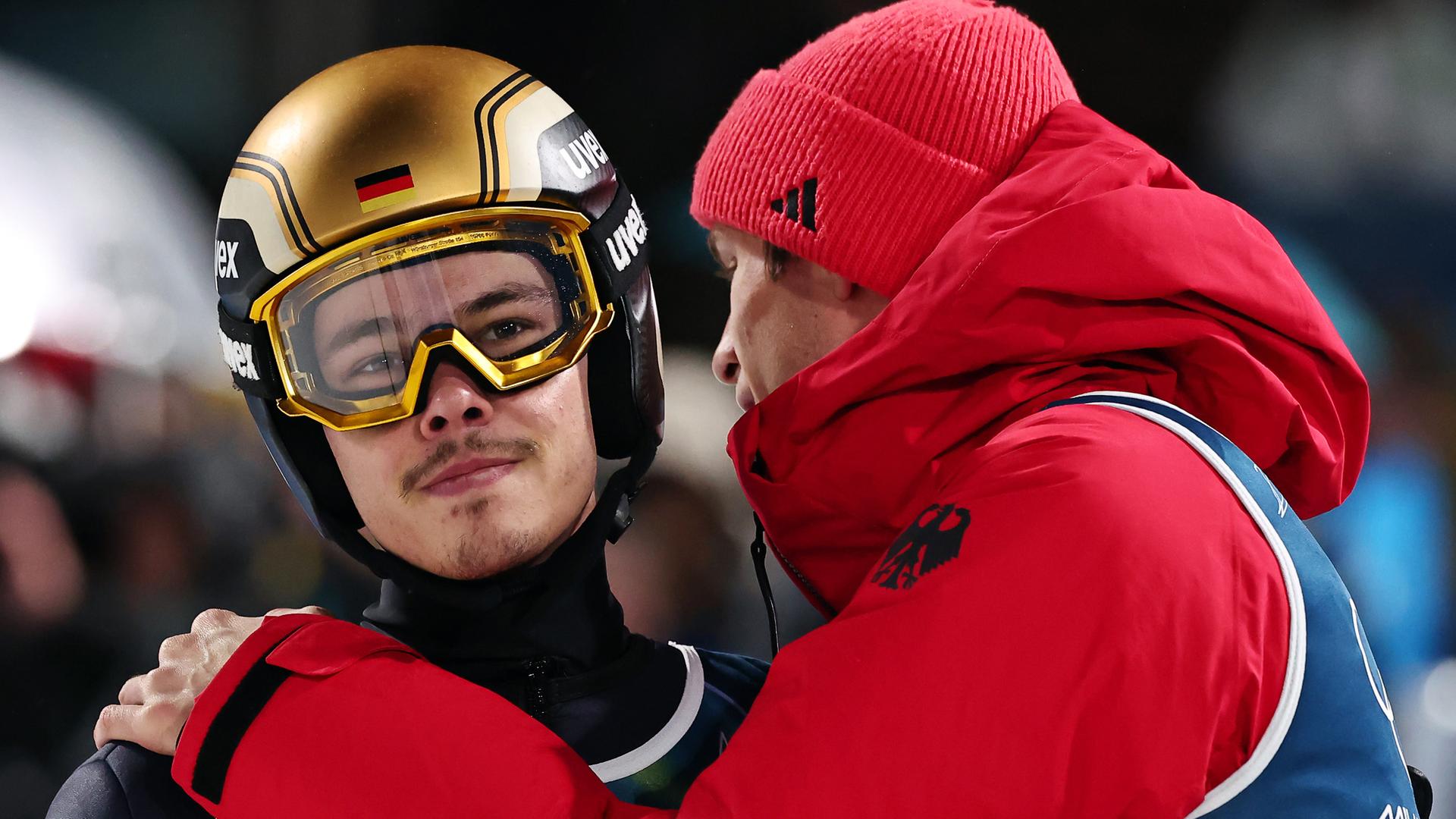 Philipp Raimund (l, Deutschland) reagiert nach seinem Sprung während der olympischen Winterspiele 2026 mit Teamkollege Andreas Wellinger (Deutschland).