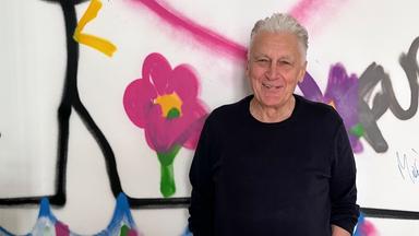 Rainhard Fendrich steht vor einer Graffitiwand.
