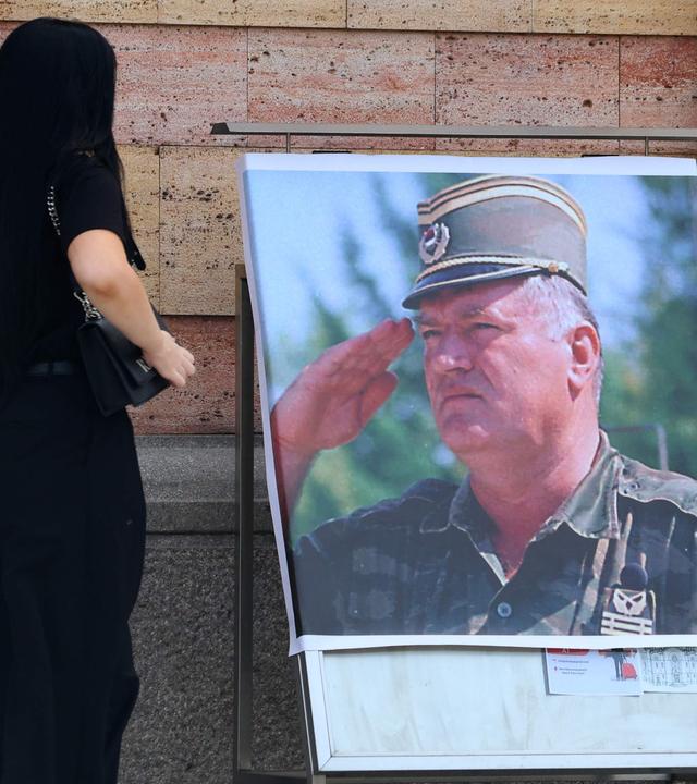Eine Frau betrachtet am 28.08.2026 vor der orthodoxen Kathedrale in Banja Luka, Bosnien, ein Plakat mit dem Bildnis des ehemaligen bosnisch-serbischen Militärchefs Ratko Mladic.