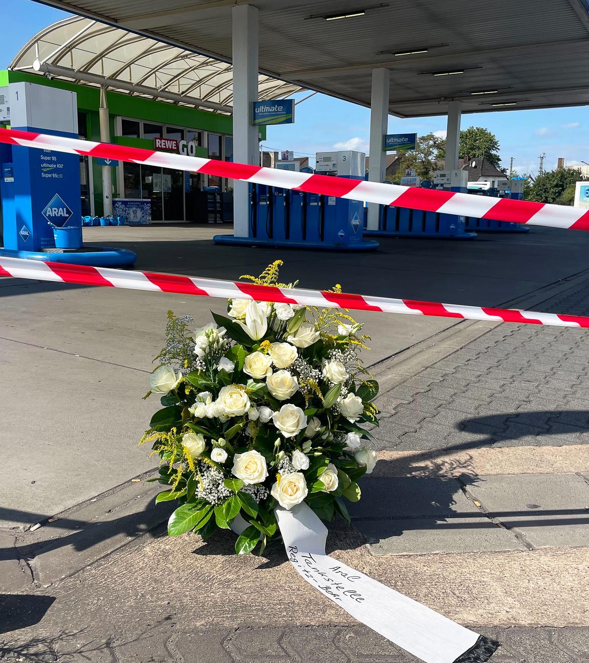 An der Tankstelle, an der nach einem Überfall ein Polizist getötet wurde, haben Mitarbeiter einen Kranz niedergelegt. Nach einem Raubüberfall auf die Tankstelle ist ein Polizist durch Schüsse getötet worden. Nach Angaben der Polizei hatte der mutmaßliche Täter dem Beamten bei einem Gerangel die Dienstwaffe entrissen und geschossen. 