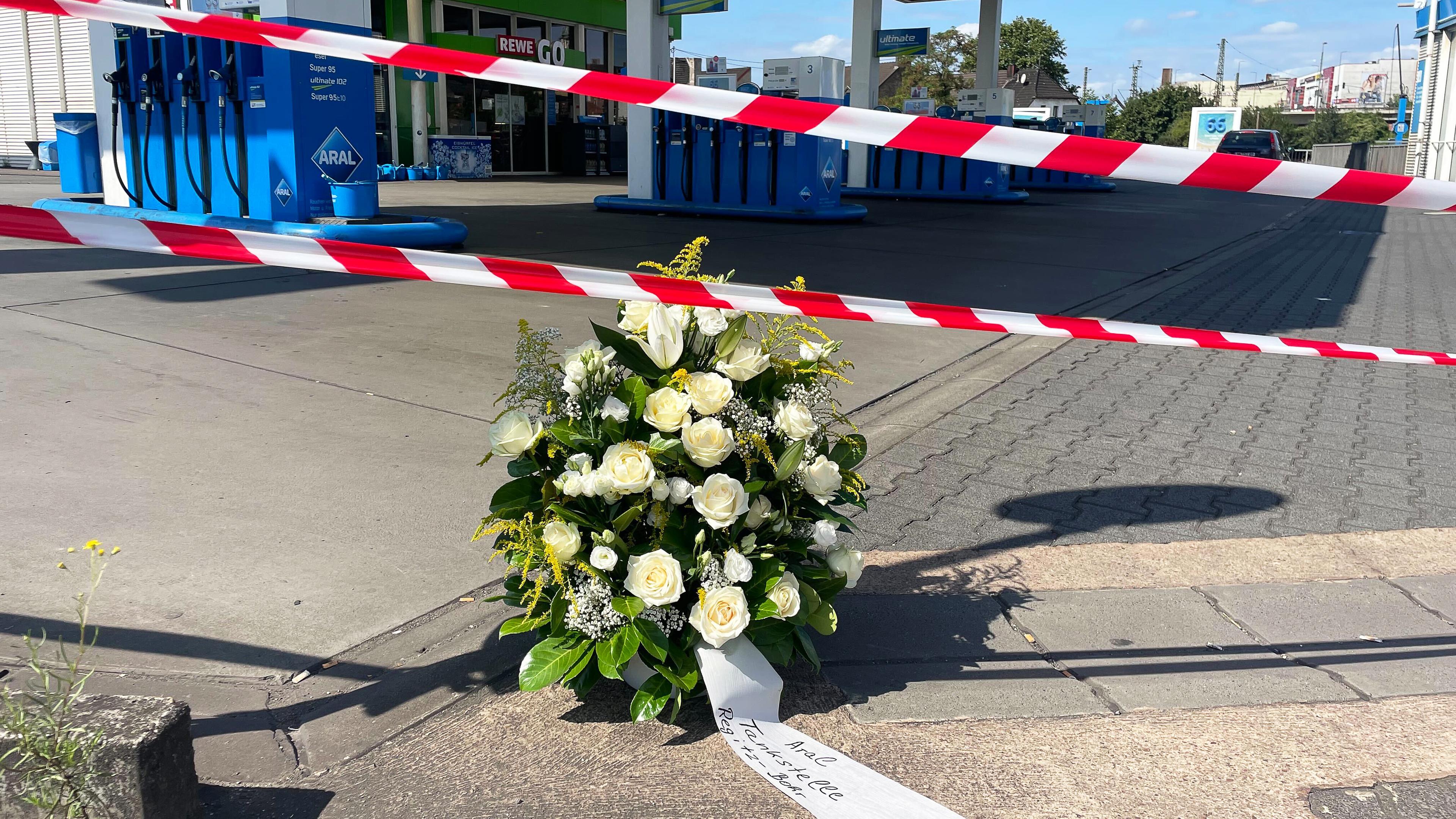 An der Tankstelle, an der nach einem Überfall ein Polizist getötet wurde, haben Mitarbeiter einen Kranz niedergelegt. Nach einem Raubüberfall auf die Tankstelle ist ein Polizist durch Schüsse getötet worden. Nach Angaben der Polizei hatte der mutmaßliche Täter dem Beamten bei einem Gerangel die Dienstwaffe entrissen und geschossen. 