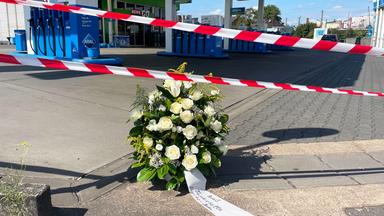 An der Tankstelle, an der nach einem Überfall ein Polizist getötet wurde, haben Mitarbeiter einen Kranz niedergelegt. Nach einem Raubüberfall auf die Tankstelle ist ein Polizist durch Schüsse getötet worden. Nach Angaben der Polizei hatte der mutmaßliche Täter dem Beamten bei einem Gerangel die Dienstwaffe entrissen und geschossen. 