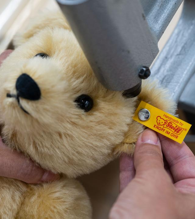 Eine Mitarbeiterin befestigt in der Produktion der Margarete Steiff GmbH einen «Knopf im Ohr», der das Markenzeichen der Steiff-Tiere ist, an einem Plüschtier.