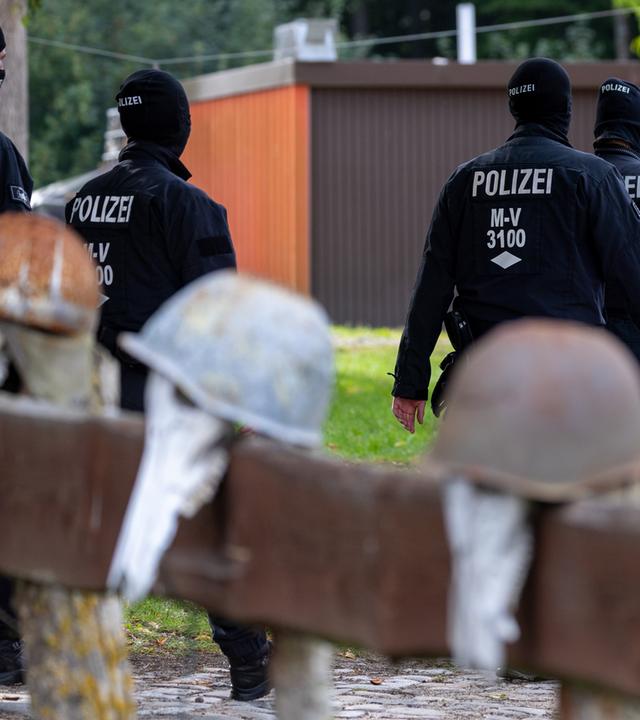Mecklenburg-Vorpommern, Jamel: Polizisten gehen zur Sicherung von Beweismittel zum Haus des bundesweit bekannter Rechtsextremist Krüger auf dessen Gartenzaun rostige Stahlhelme hängen.