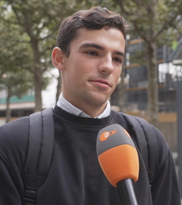 Zu sehen ist ein junger Mann in der Stadt, der interviewed wird