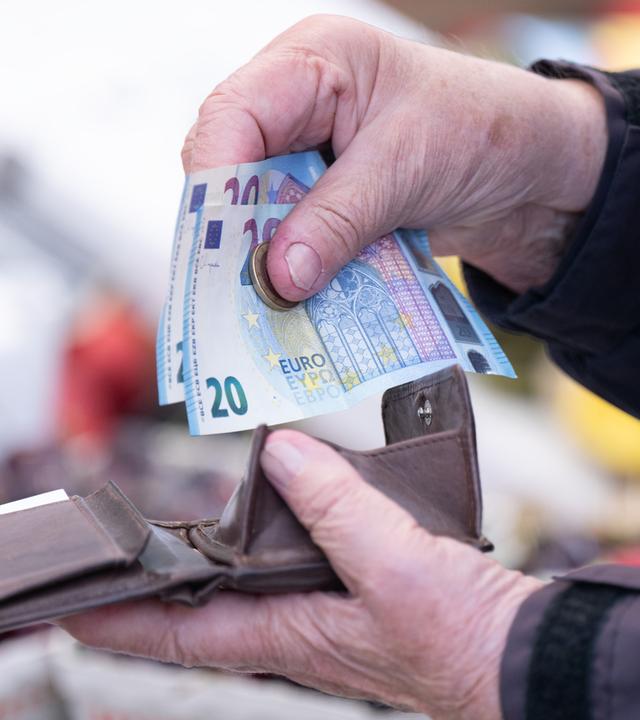 Eine Frau sortiert auf einem Wochenmarkt das Wechselgeld für ihre Einkäufe in ein Portemonnaie.