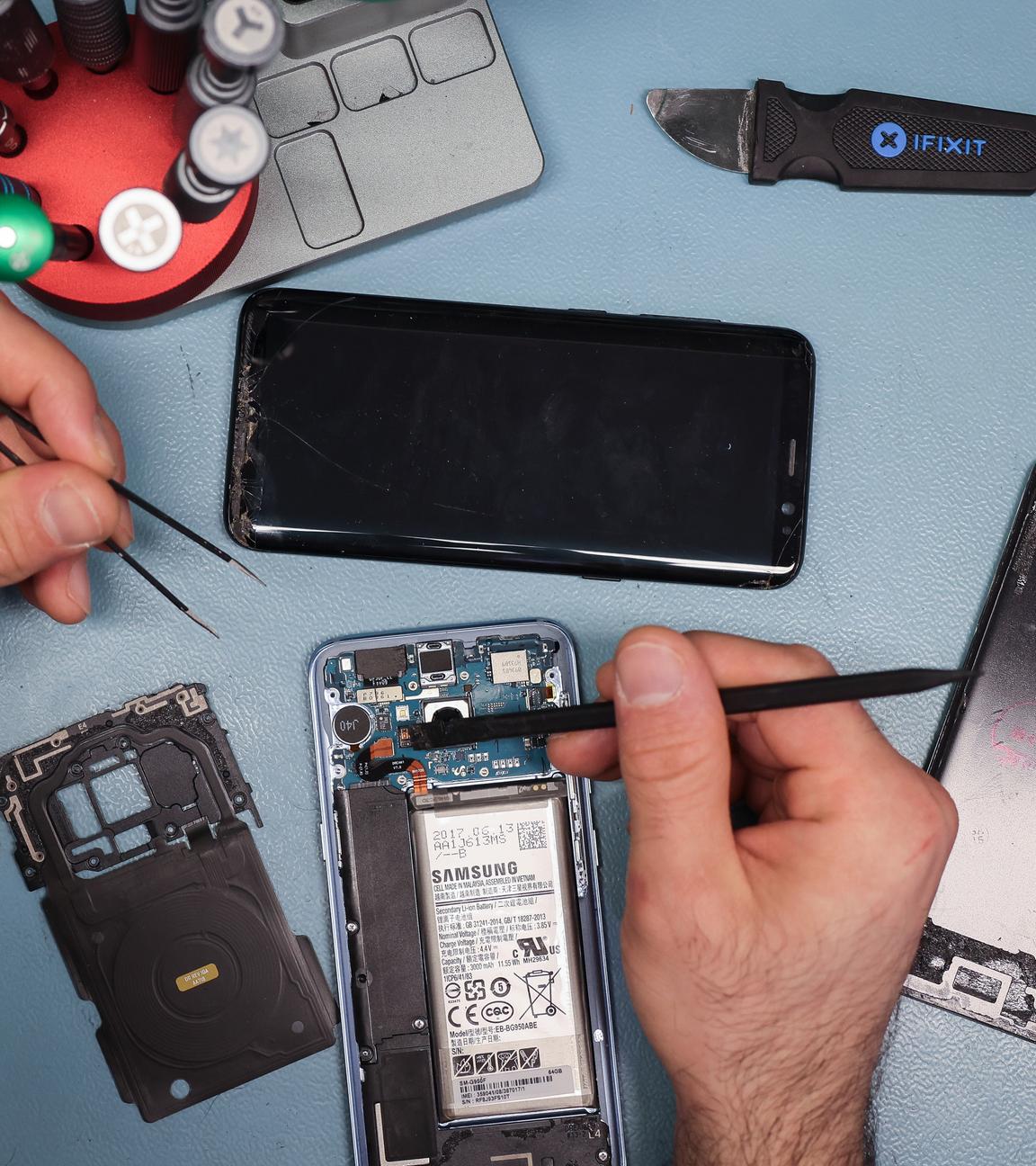  Ein Techniker arbeitet an einem Smartphone mit defektem Display in seinem kleinen Fachgeschäft für Reparaturen und Zubehör. 