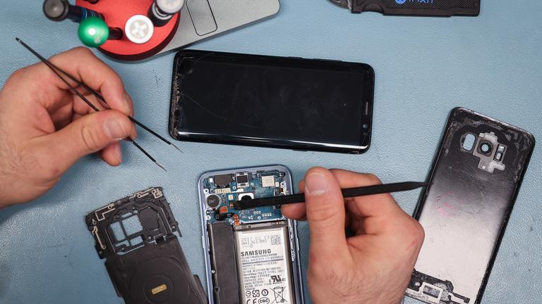  Ein Techniker arbeitet an einem Smartphone mit defektem Display in seinem kleinen Fachgeschäft für Reparaturen und Zubehör. 