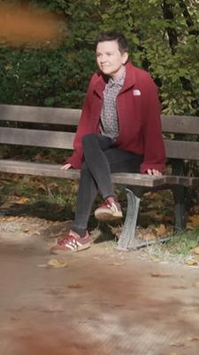 Zu sehen ist Eva-Maria Wild auf einer Bank in einem Park. 