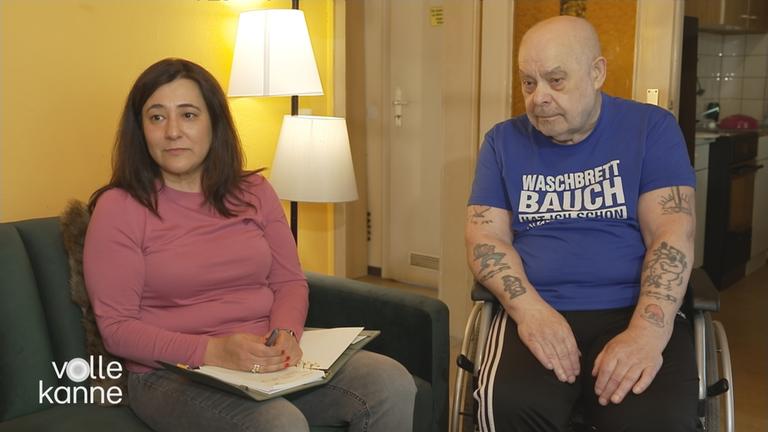 Rechtliche Betreuerin (links) sitzt auf einer Couch und der rechtlich Betreute (rechts) sitzt im Rollstuhl daneben.