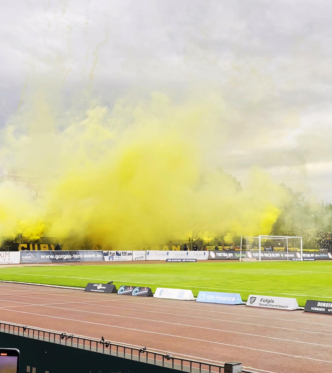 Rechtsextreme Fans nebeln das Stadion von Alemannia Aachen ein. Auf einer Seite des Sportplatzes steigt gelber Rauch auf.