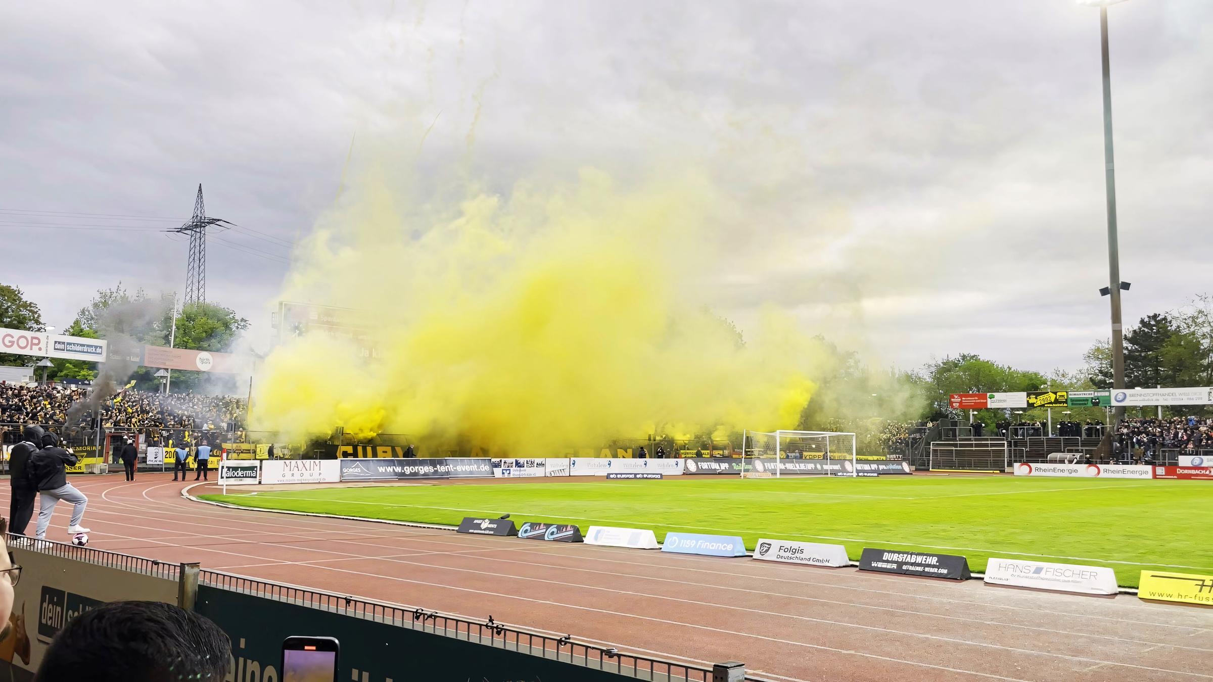 Rechtsextreme Fans nebeln das Stadion von Alemannia Aachen ein. Auf einer Seite des Sportplatzes steigt gelber Rauch auf.
