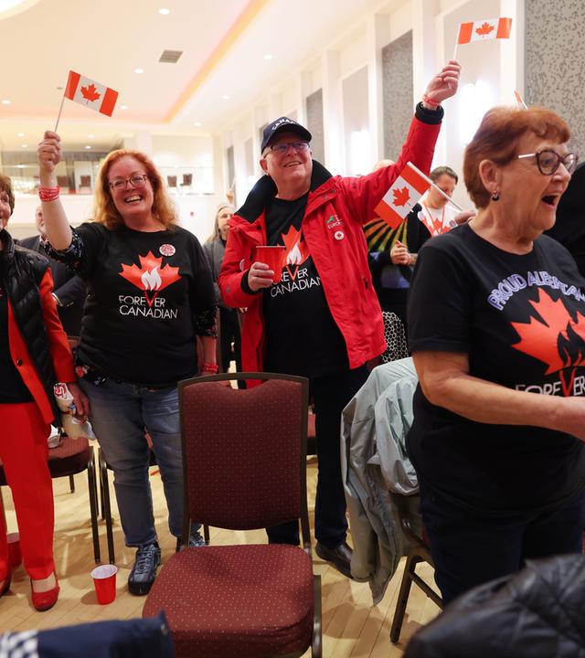 Mehrere Menschen auf einer Pro-Kanada-Wahlparty halten kleine Kanada-Fahnen in die Höhe und jubeln. 