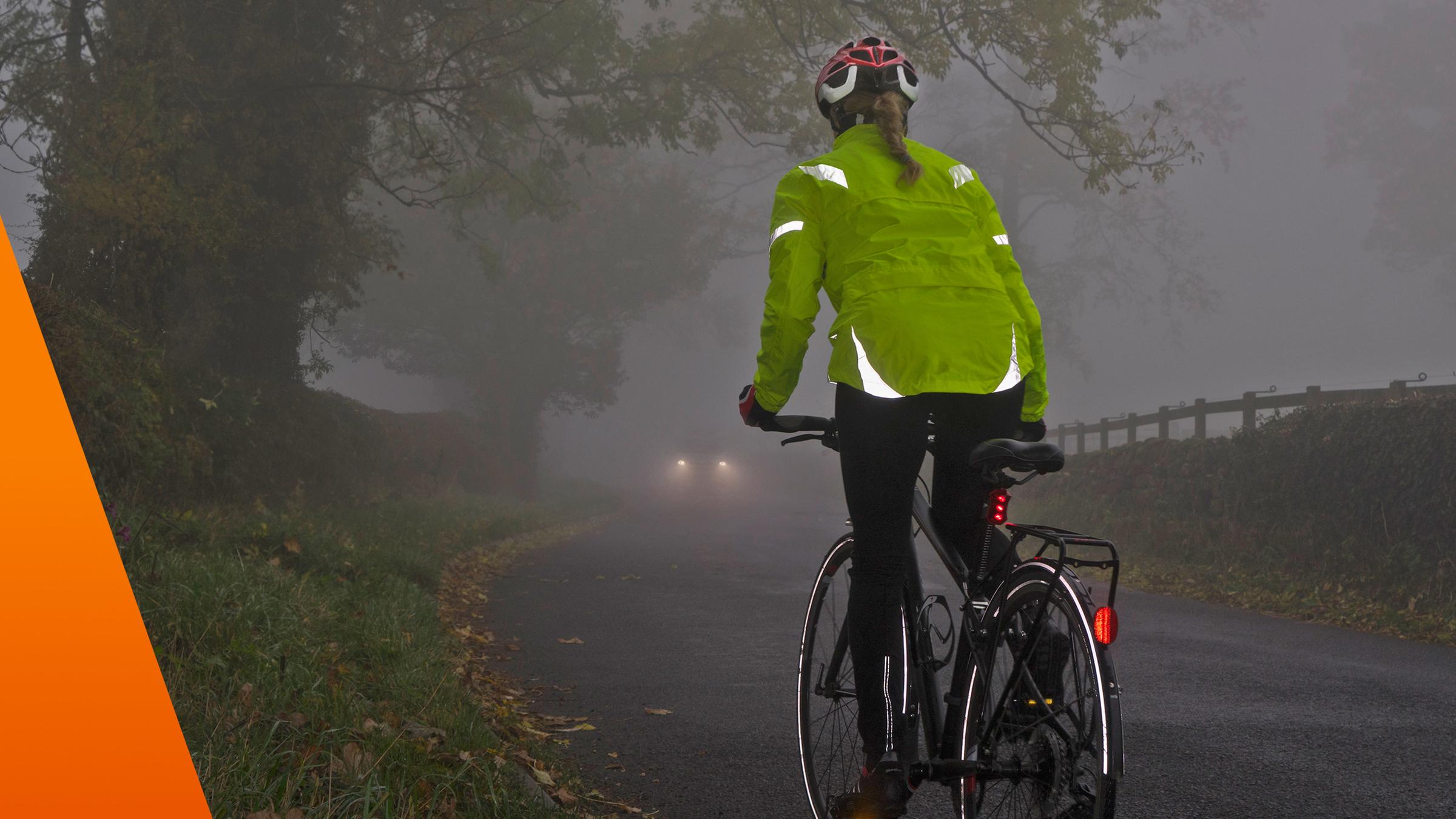 Frau fährt im Dunkeln Fahrrad und hat eine reflektierende Jacke an