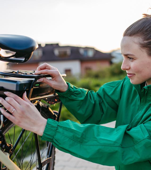 Frau in grüner Outdoor-Jacke prüft den Akku an ihrem E-Bike