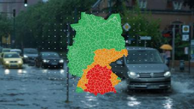 Autos fahren über eine überflutete Straße. Davor liegt eine Karte mit den aktuellen Regen-Warnungen des DWD