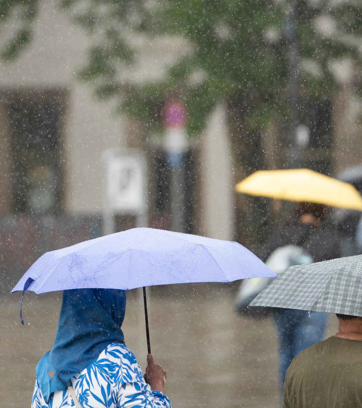 Baden-Württemberg, Stuttgart: Menschen mit Schirmen gehen bei Regen durch Stuttgart.
