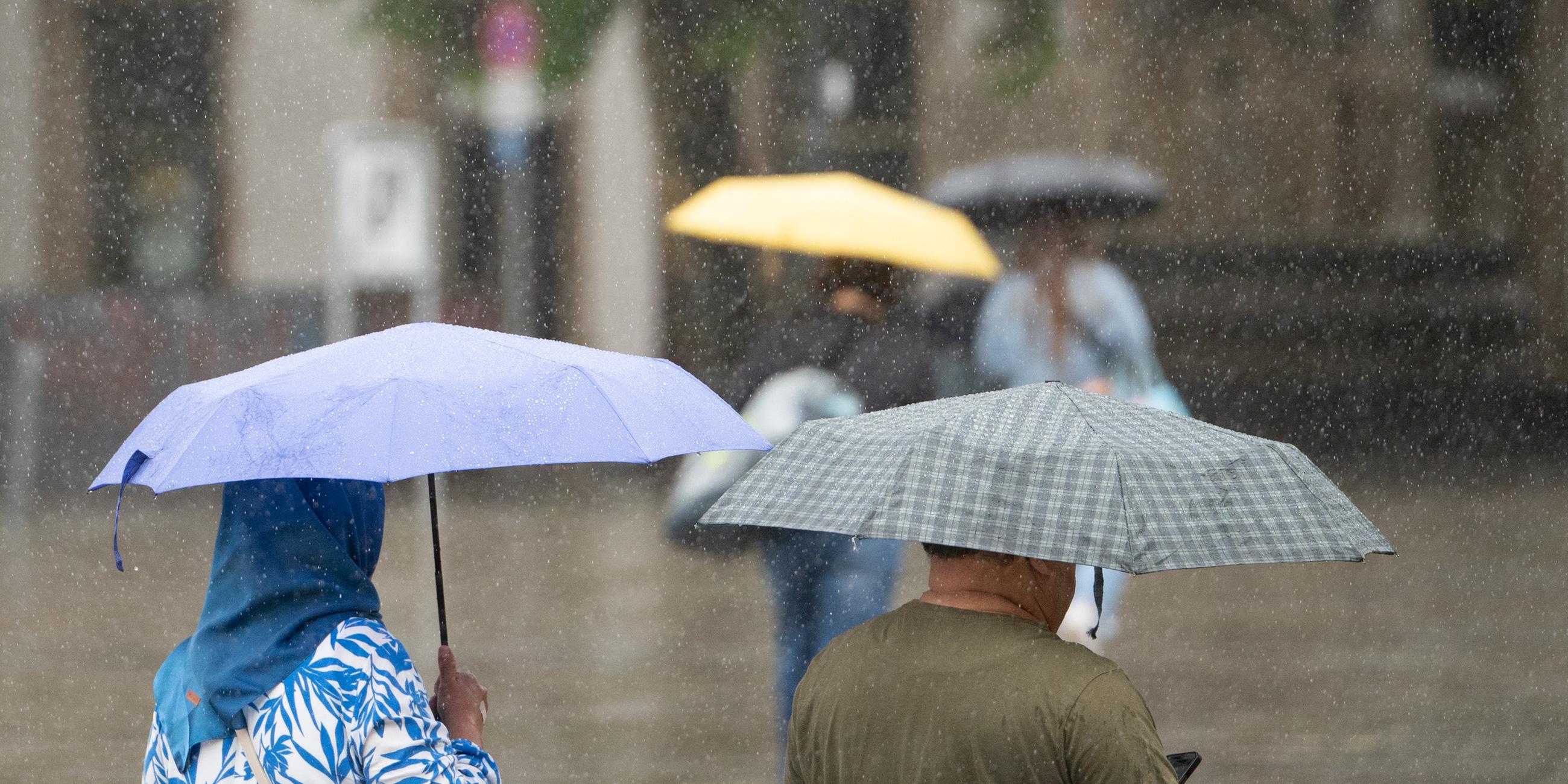 Baden-Württemberg, Stuttgart: Menschen mit Schirmen gehen bei Regen durch Stuttgart.