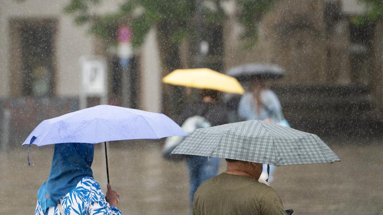 Baden-Württemberg, Stuttgart: Menschen mit Schirmen gehen bei Regen durch Stuttgart.