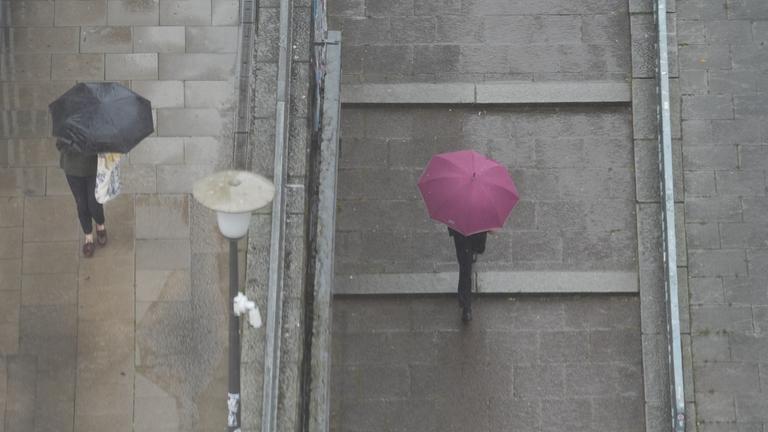 Passanten gehen mit Regenschirmen im strömenden Regen durch die Innenstadt.