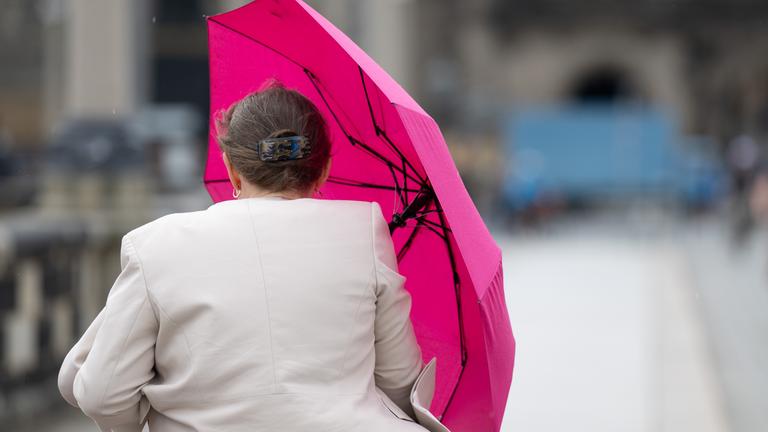 Eine Frau hält einen pinkfarbenen Regenschirm, während sie über die Augustusbrücke in Dresden geht.