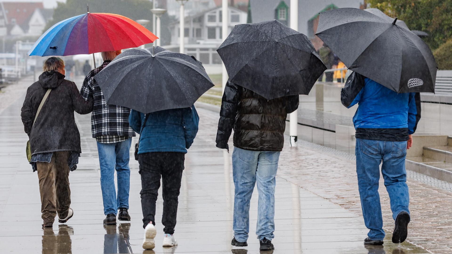 Ausflügler gehen im Regen unter Schirmen auf der Promenade von Travemünde. 