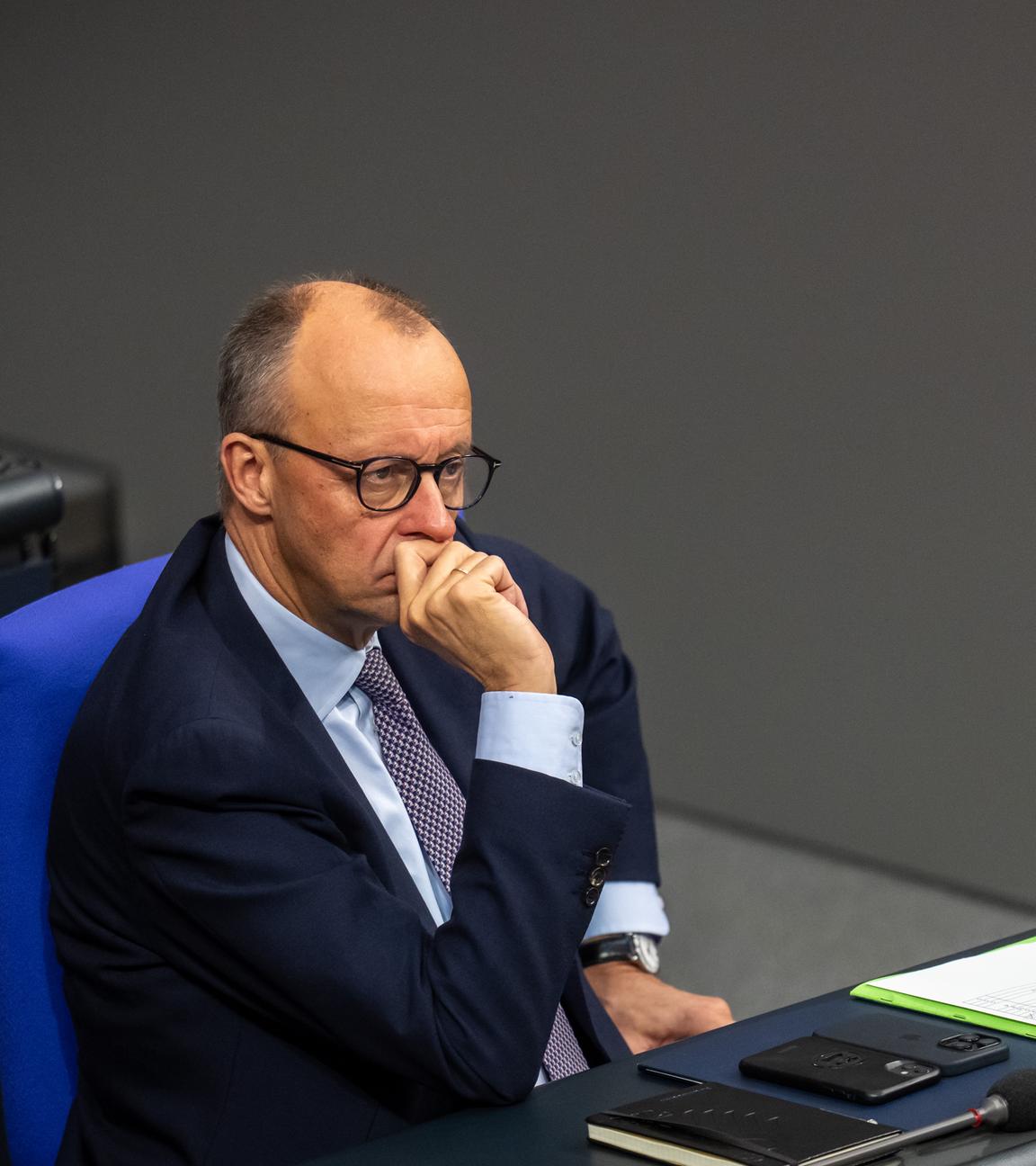 Der Bundeskanzler Friedrich Merz ist zu sehen im Bundestag. Er sitzt und schaut nachdenklich.