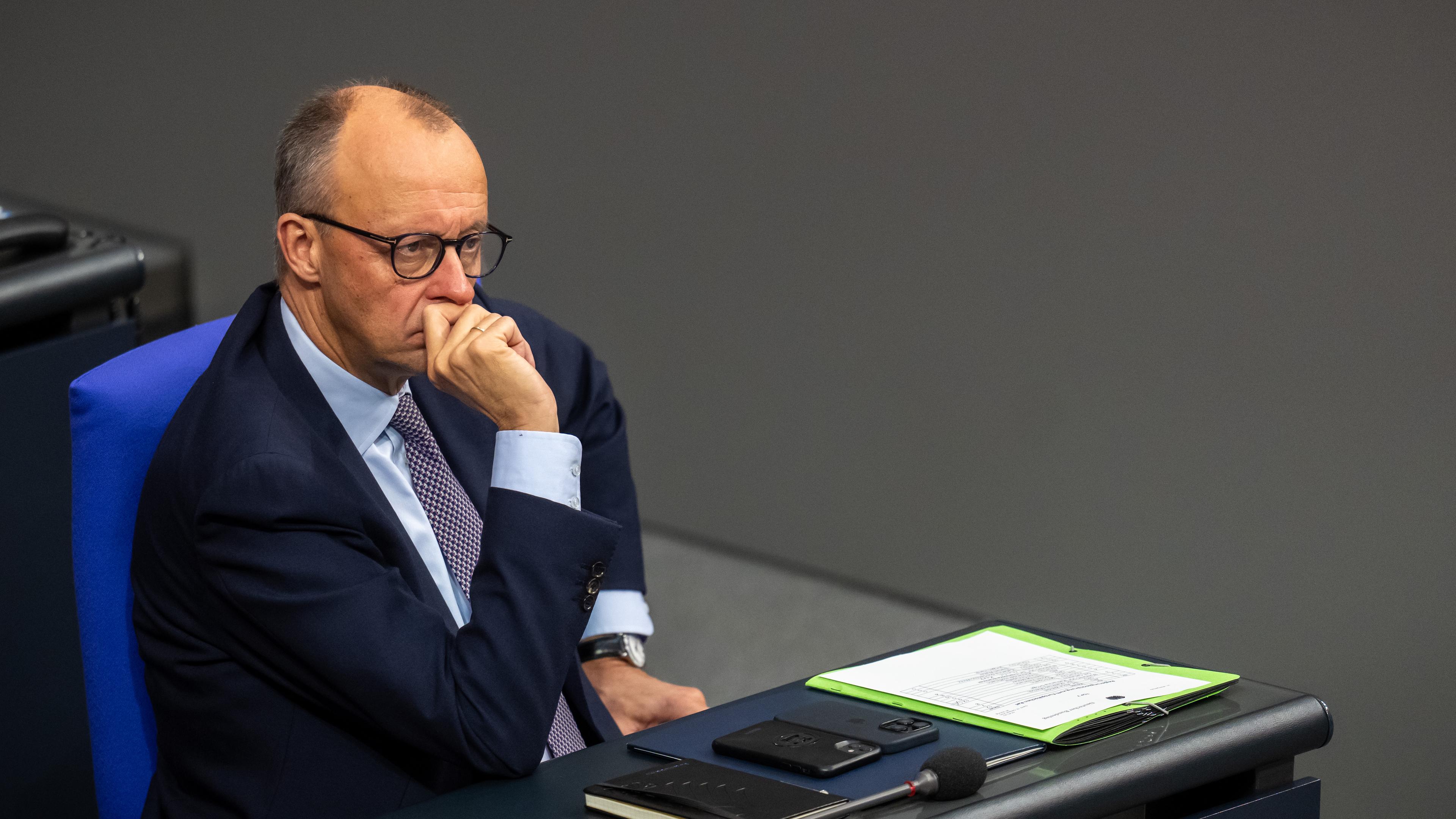 Der Bundeskanzler Friedrich Merz ist zu sehen im Bundestag. Er sitzt und schaut nachdenklich.