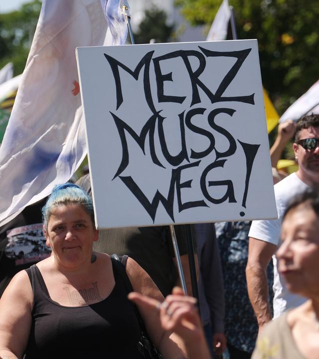 Sachsen, Plauen: Eine Teilnehmerin einer Demonstration des "Projekt M1llion" hält ein Plakat mit der Aufschrift "Merz muss weg!".