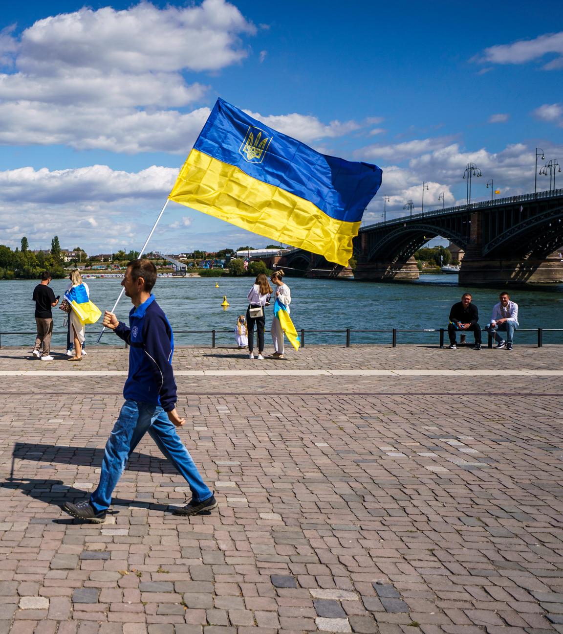 Archiv: Ein Mann geht auf einer Kundgebung zum 34. Unabhängigkeitstag der Ukraine mit der ukrainischen Nationalflagge am Rheinufer.