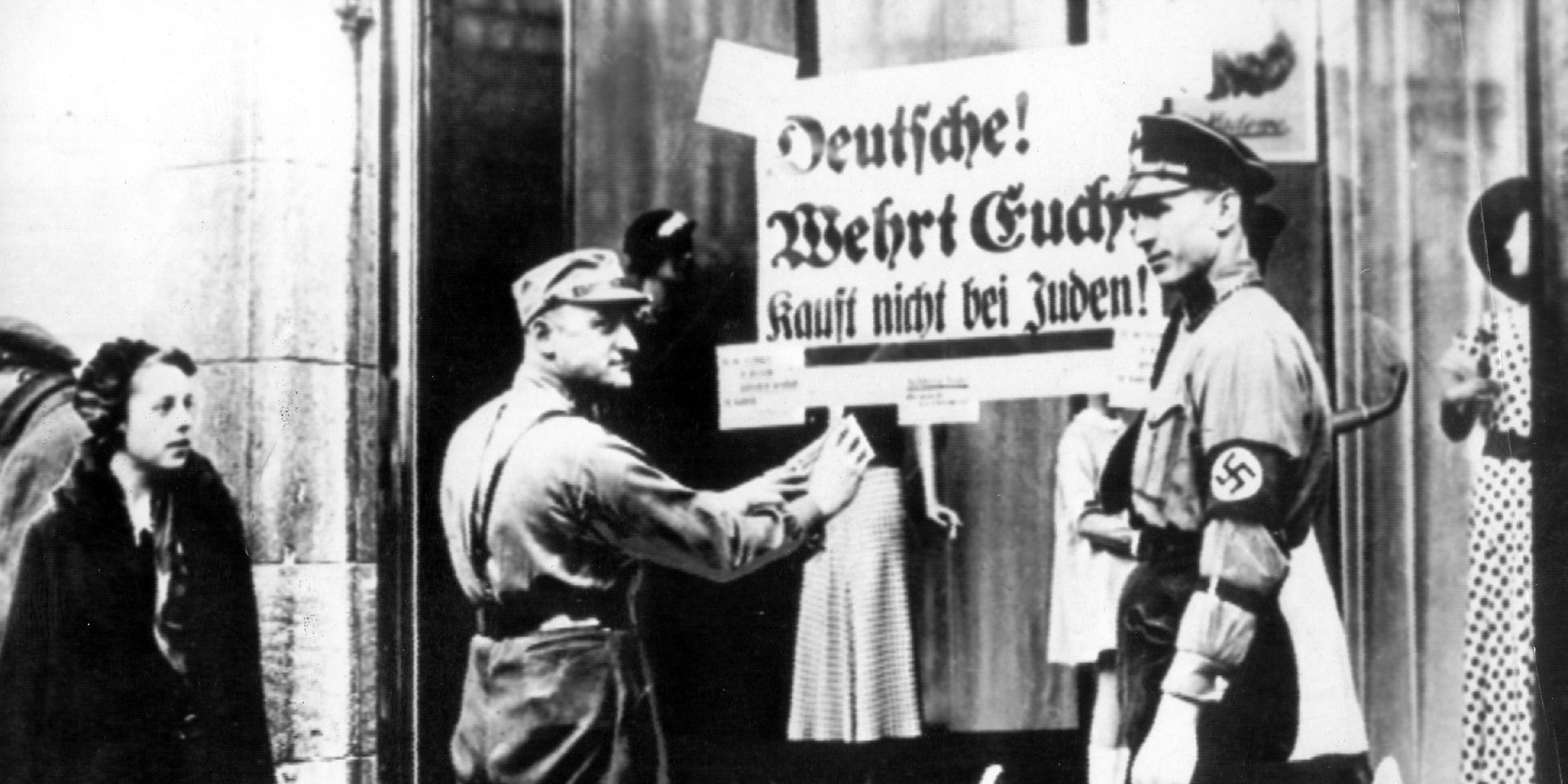 SA Männer kleben Plakate an Geschäfte mit der Aufschrift: "Deutsche wehrt euch! Kauft nicht bei Juden!"