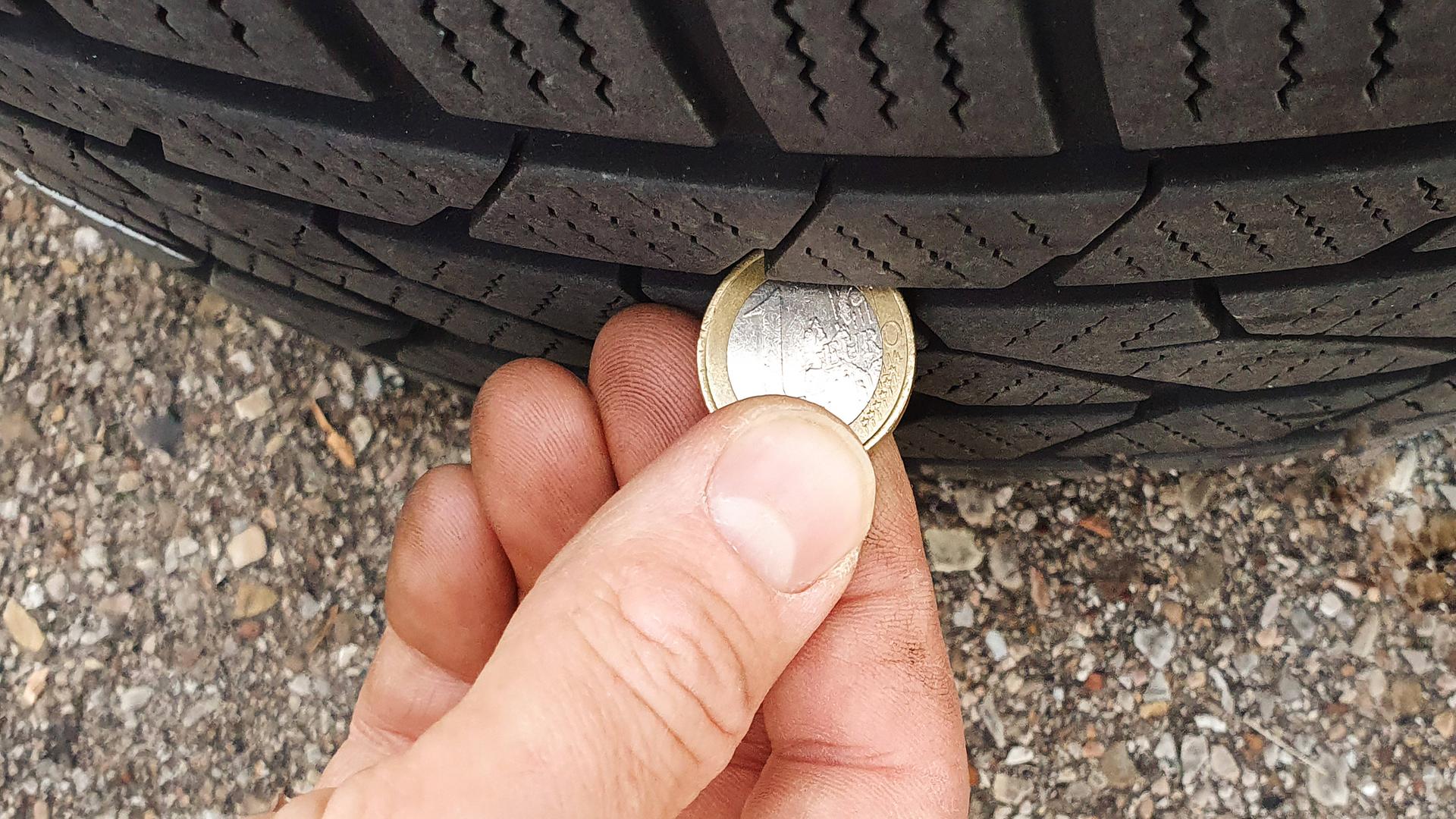 Ein Mann hält eine Euro-Münze an einen Autoreifen, um die Profiltiefe zu überprüfen.