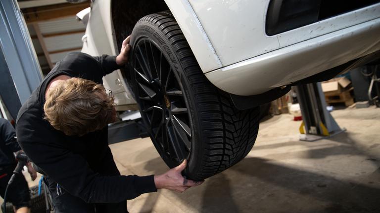 Ein Kfz-Mechaniker montiert ein Rad an einem Pkw.