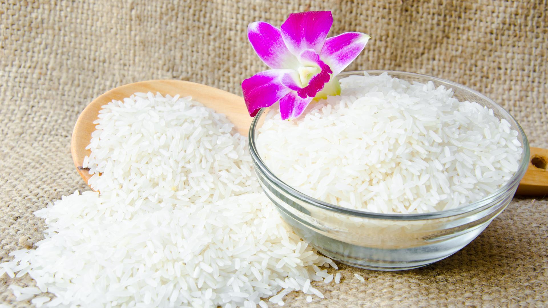Eine Schüssel mit gekochtem Jasmin-Reis und einem Holzlöffel im Hintergrund.