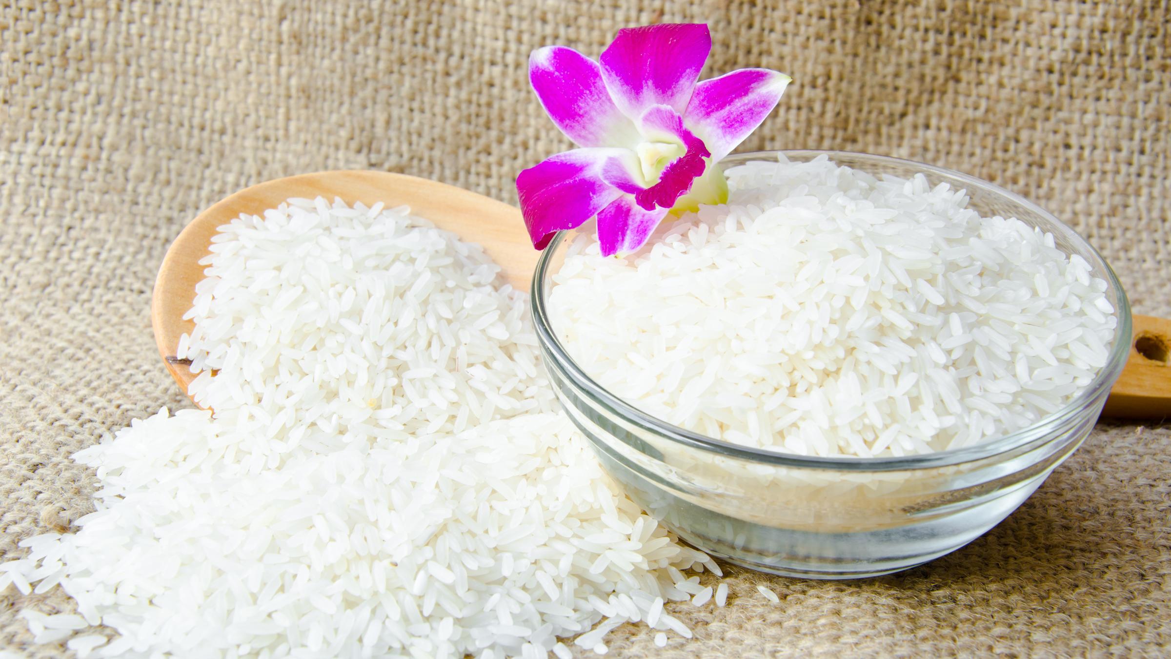 Eine Schüssel mit gekochtem Jasmin-Reis und einem Holzlöffel im Hintergrund.