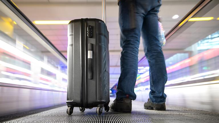 Ein Reisender steht mit seinem Koffer auf einem Fahrsteig des Flughafens München am 12.04.2019